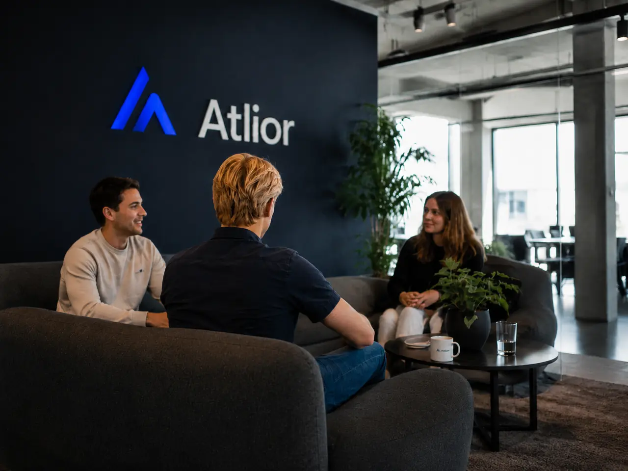 Drie mensen in gesprek in het kantoor van Atlior, met het Atlior-logo op de wand